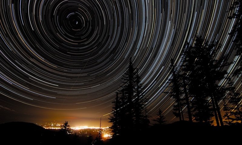 Обои ночь, деревья, звезды, город, star trails, night, trees, stars, the city разрешение 1920x1200 Загрузить